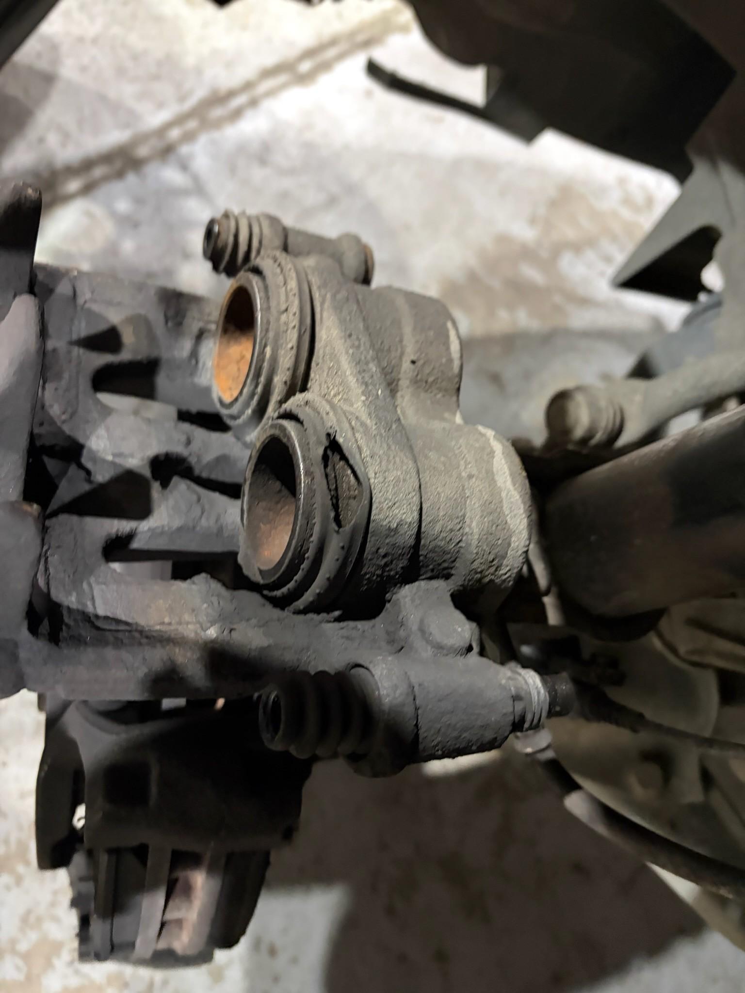Worn brake caliper with torn dust boot and rusty pistons