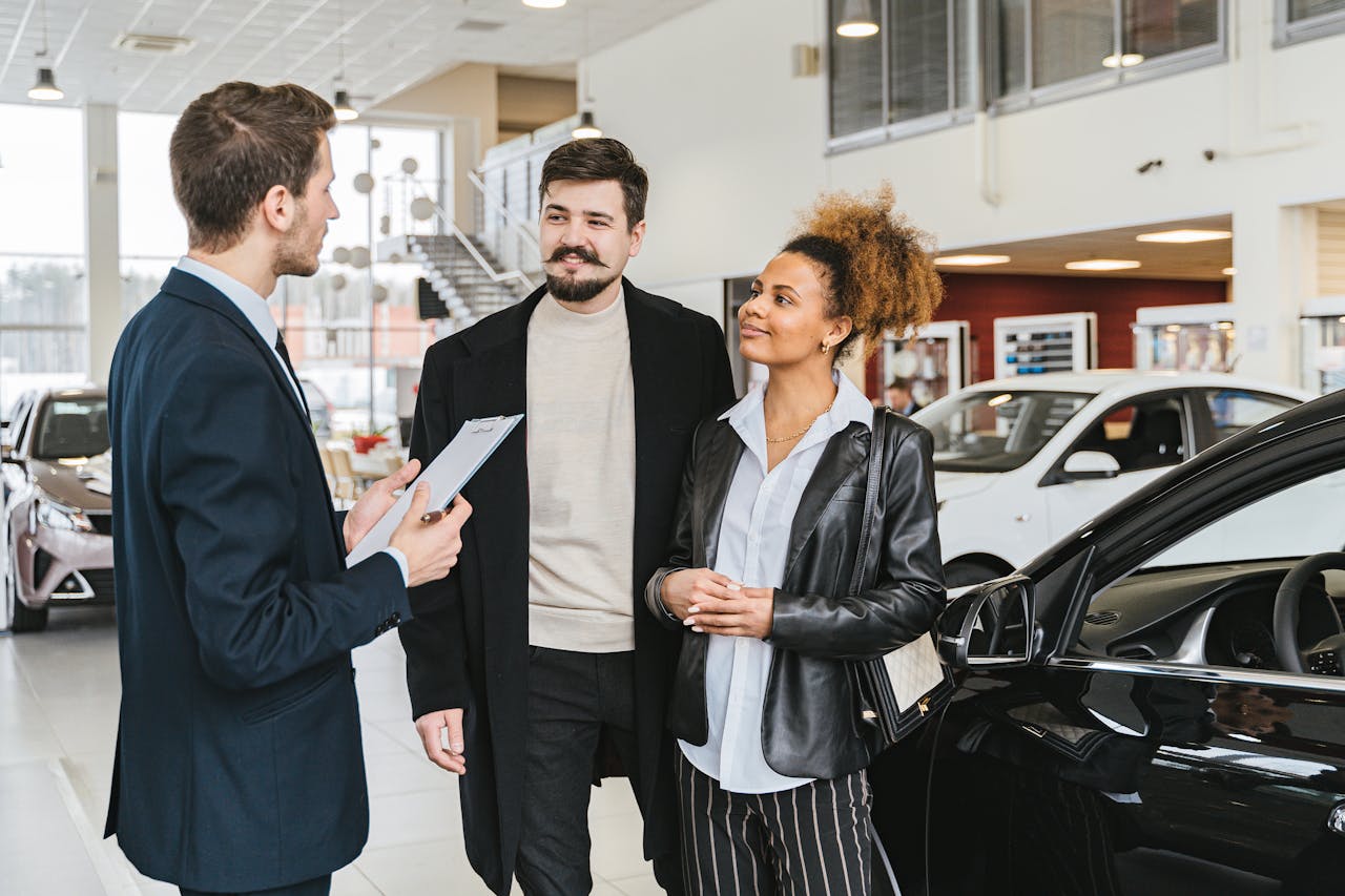 A car salesman with a clipboard talking to a couple beside a car in a dealership