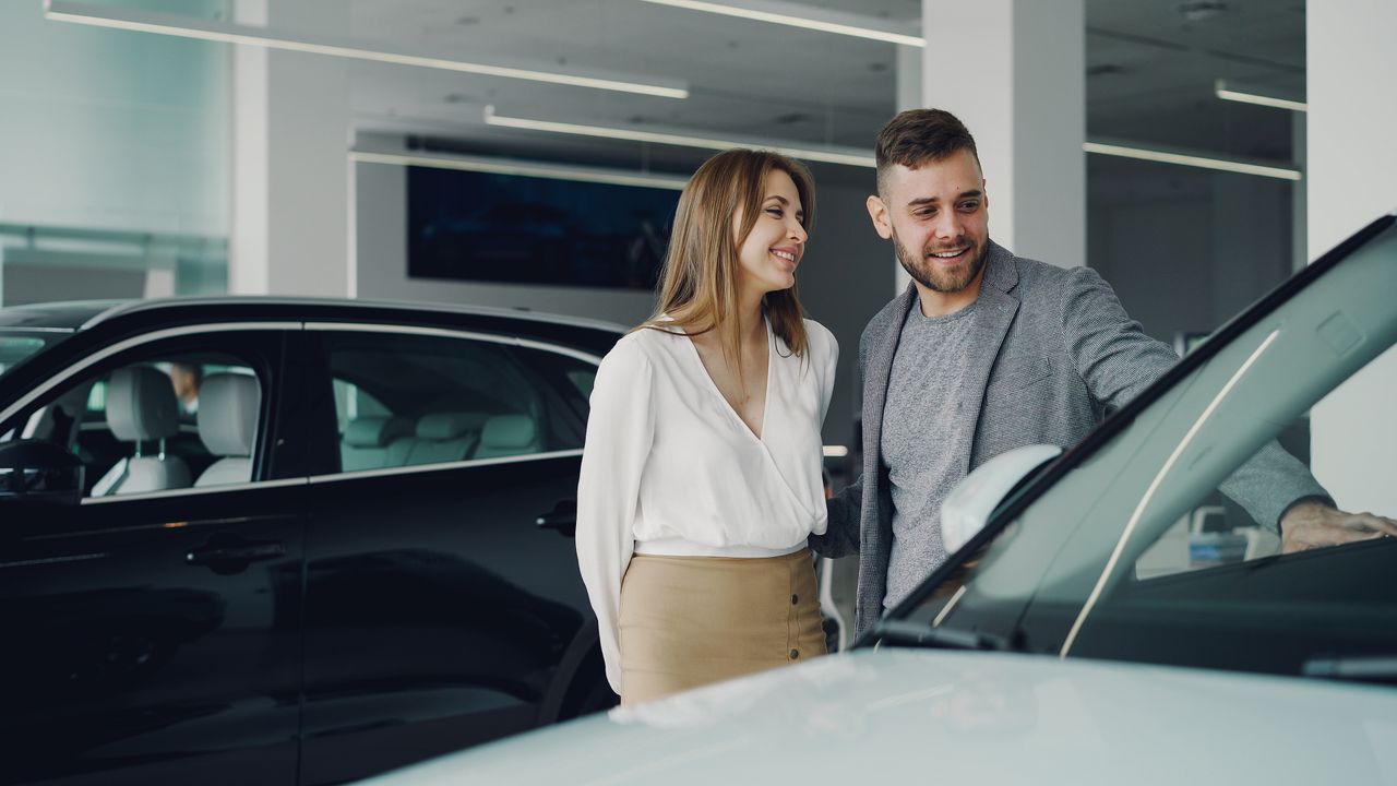 A couple looking closely at a used car in a showroom before buying